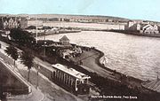 An old photograph of a tram running along a waterfront road.