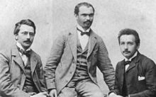 Three young men in suits with high white collars and bow ties, sitting.