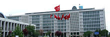 A mid-rise glass-paned office building, with an array of Turkish flags in the front.