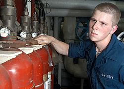 a sailer in coveralls wipes down red gas bottles
